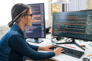 Female freelance developer coding and programming. Coding on two with screens with code language and application.