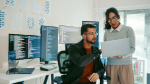 Two Hispanic programmers reviewing code on a laptop in a modern office